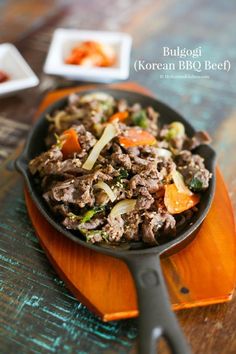 a skillet filled with meat and vegetables on top of a wooden table