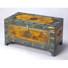 an old wooden box is painted yellow and blue with gold accents on the top, sitting on a white surface