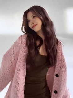 a woman with long dark hair wearing a pink cardigan