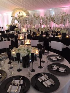 the table is set up with black and white plates, silverware, candles and centerpieces