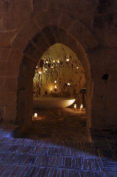 a bathtub with candles in it is lit by the light from an arched window