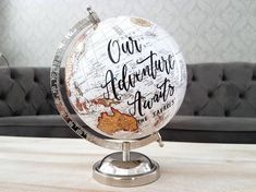 a globe with the words our adventure awaits on it sitting on a table in front of a couch