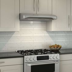 a bowl of fruit sitting on top of a stove in a kitchen next to white cabinets