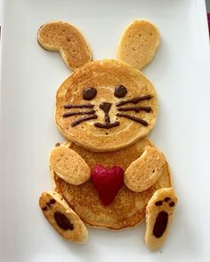 a bunny made out of pancakes on a plate with raspberries in the shape of a heart