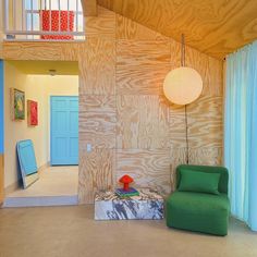 a green chair sitting in front of a blue door next to a wooden wall and window