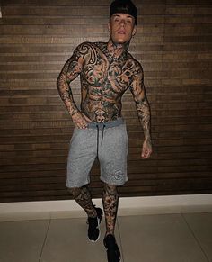 a man with tattoos standing in front of a wall