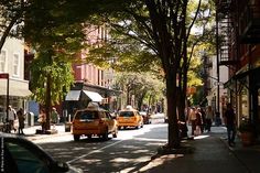 a taxi cab driving down a street next to tall buildings with trees on both sides