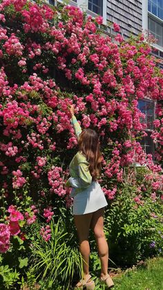 a woman is standing in front of pink flowers and reaching up into the air with her hand