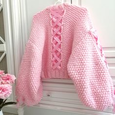 a pink knitted sweater hanging on a white coat rack with flowers in the foreground