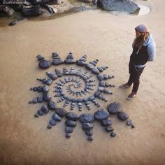 a woman standing in front of a circular sculpture made out of rocks on the ground