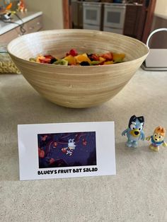 a bowl of fruit next to a small toy figurine and a business card