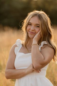 a woman in a white dress is posing for a photo with her hand on her chin