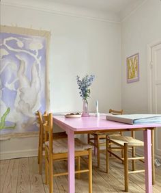 a pink table and chairs in a room with a painting on the wall behind it