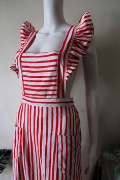 Pretty Vintage Fenno-Sport apron dress from the 1970s. Comfortable cotton blend fabric with irregular red stripes on white background. Midi length, elasticated waist. Large ruffles along the shoulder straps. The straps are crossed over in the back and attached to the waistband with buttons (length adjustable). Two patch pockets on the front. Wide skirt with ruffle hem. Unlined.  Made in Finland! Perfect for a summer vacation! Looks great with a white top or t-shirt underneath and a pair of sanda Skirt With Ruffle Hem, Wide Skirt, Vacation Looks, Apron Dress, Red And White Stripes, Red Fabric, Dress Clothes For Women, White Top, Ruffle Hem