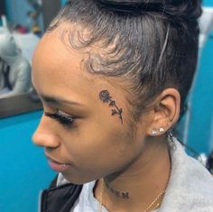 a woman with a flower tattoo on her forehead and behind her ear, sitting in a hair salon