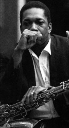 a man in a suit and tie holding a saxophone to his mouth while sitting down