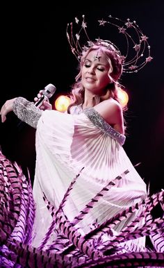 a woman in a white dress holding a microphone and wearing a crown on her head