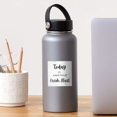 a gray water bottle sitting on top of a wooden table next to a white laptop