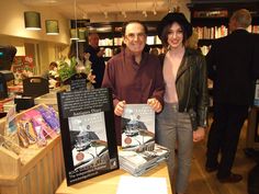 a man and woman standing next to each other in front of a table with books on it