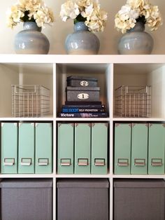 three vases with flowers are sitting on top of bookshelves in a room