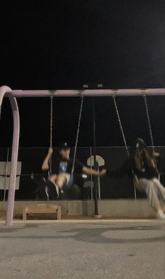 two people sitting on swings in the dark, one is falling off his skateboard