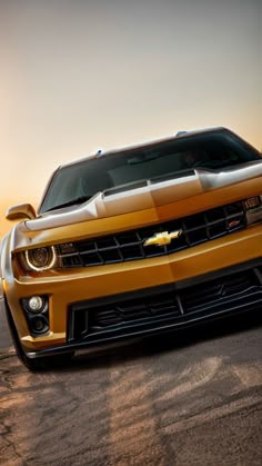 the front end of a yellow chevrolet camaro parked on a desert road at sunset