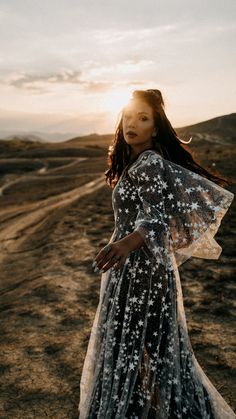 a woman standing in the middle of a dirt road wearing a dress with stars on it