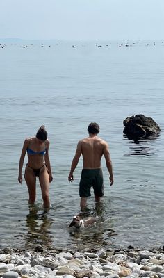 two people standing in the water near rocks