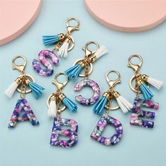 six different key chains with letters and tassels hanging from them on a blue surface