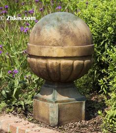 a statue in the middle of a garden with purple flowers around it and bushes behind it