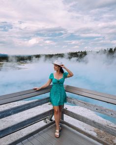 a woman in a green dress standing on a boardwalk next to a geyser