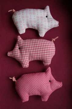 three stuffed pigs sitting next to each other on a red cloth covered surface with pegs