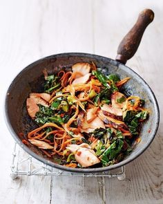 a wok filled with vegetables and meat on top of a wooden table