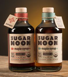 two bottles of syrup sitting on top of a wooden table next to each other, one containing sugar moon and the other containing maple syrup