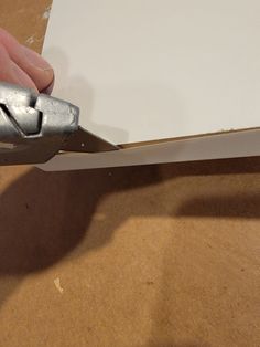 a person cutting paper with a pair of scissors on top of the piece of plywood