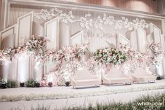 a stage set up with white couches and flowers on the wall, along with floral centerpieces