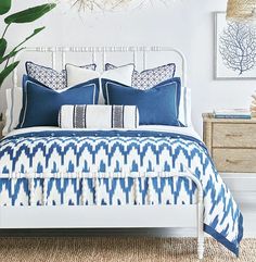 a white bed topped with blue and white pillows next to a potted green plant