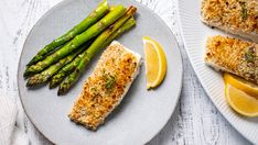 fish and asparagus on a plate with lemon wedges next to the dish