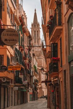 a narrow street with buildings and signs on the sides, in front of a church steeple