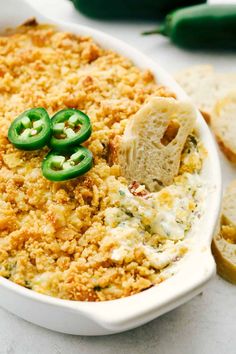 a casserole dish with green peppers and cheese on top, next to slices of bread