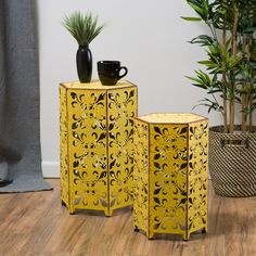 two yellow side tables sitting on top of a wooden floor next to a potted plant