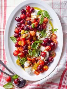 a white plate topped with cherry tomatoes and mozzarella cheese on top of a red checkered table cloth