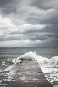 an ocean view with waves crashing on the end of a pier and dark clouds in the sky