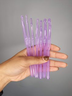 a woman's hand holding several purple plastic toothbrushes