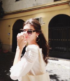 a woman walking down the street with her hand on her face while wearing sunglasses and a white dress