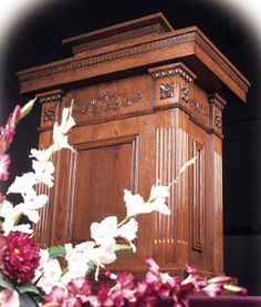 a tall wooden clock tower sitting next to flowers on top of a purple table cloth