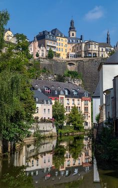 buildings on the side of a river with trees in front of it and a hill behind them