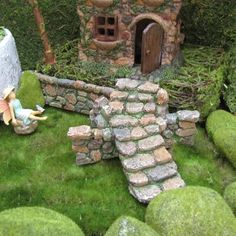 a fairy garden with moss growing on the ground and a small house in the background