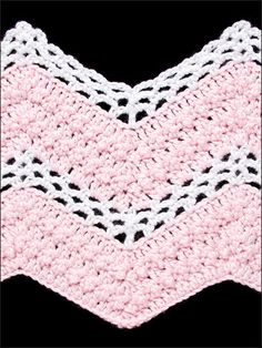 a crocheted pink and white blanket on top of a black surface with an arrow in the middle