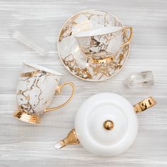 marble tea set with gold trimmings on white wooden table top next to cup and saucer